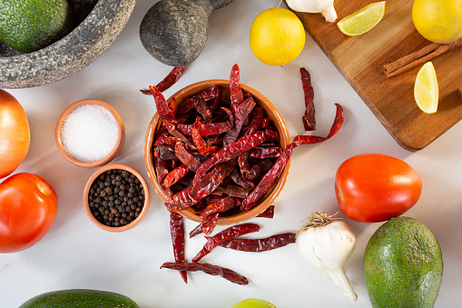 A top down view of a spilled bowl of dried chile de arbol, among other salsa ingredients.