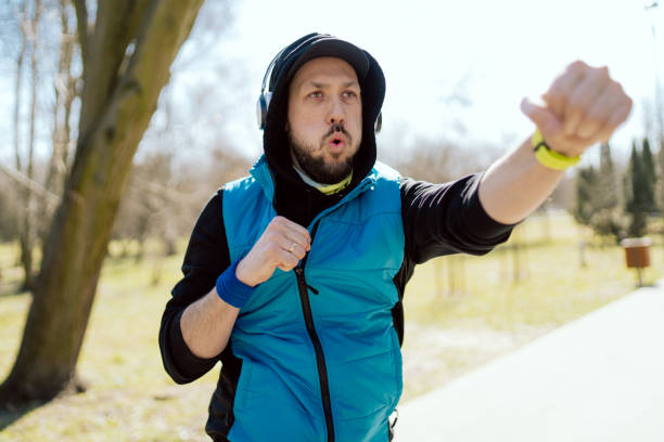 Man warms up before morning run, workout, warmly dressed guy in helmet sweatshirt and vest, headphones on ears, athlete spends time in public park.