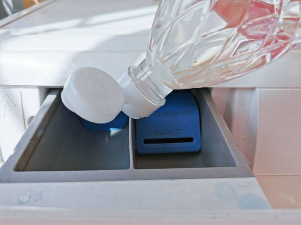Close up hand pouring the vinegar into the front-loading drawer. Clean a washing machine with vinegar.