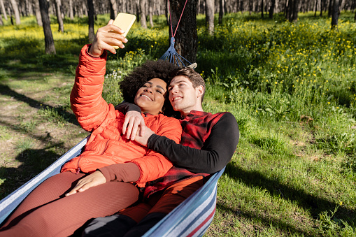friends relax in a hammock in the woods while taking photos