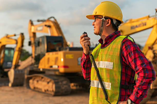 los ingenieros asiáticos utilizan walky talky con el equipo para el proyecto de movimiento de tierras por excavadora. capataz usa computadora portátil para proyecto de construcción excavadora pesada. maquinaria y equipo para trabajadores industriales. - pesado fotografías e imágenes de stock