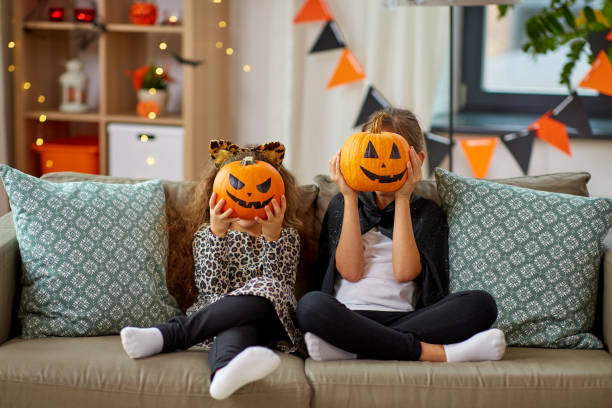 girls in halloween costumes with pumpkins at home stock photo