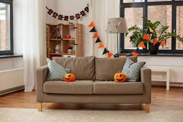 holidays, decoration and party concept - home room with jack-o-lanterns or pumpkins on sofa and halloween decorations