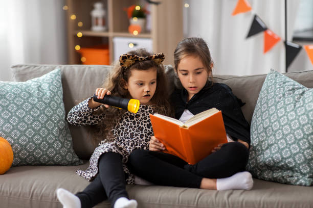 девочки в костюмах на хэллоуин читают книгу дома - leopard 2 стоковые фото и изображения