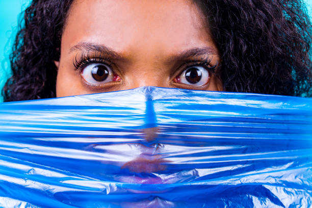 unhappy female with plastic bag on her head against blue wall studio .