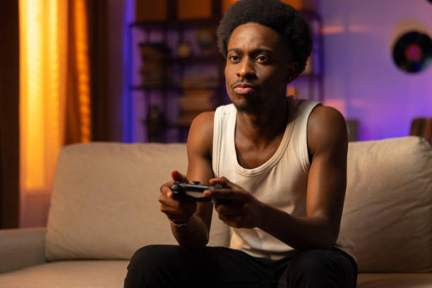 istock A focused afro man plays a video game on a console. A lone guy is sitting in home clothes holding a pad in hands. Male entertainment in spare time 1392273059