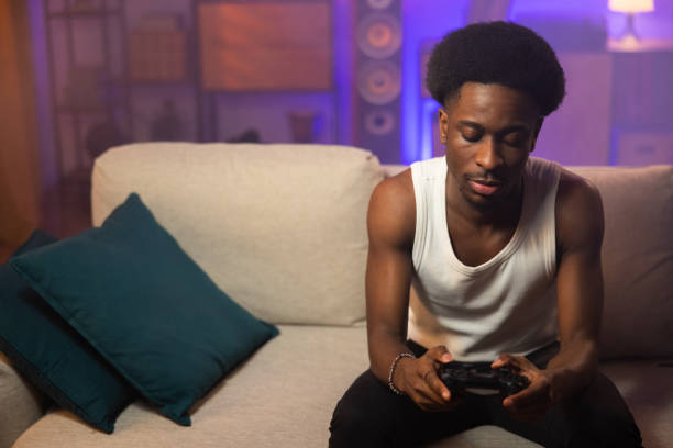 istock An Afro man has broken up with girlfriend and is spending the weekend alone at home. The student is sadly occupying time playing games on the console, holding the pad in hands reluctantly 1392273266