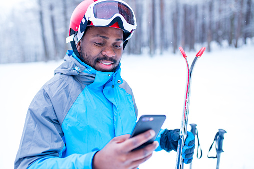 afro american man in blue jacket run ski outdoors in freeze forest holding a phone on hands