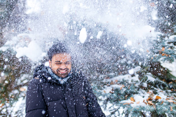indian man enjoying snowflakes falling from upwards in forest.