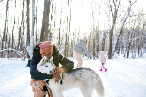 mixed race man hug his dog husky in winter forest park.