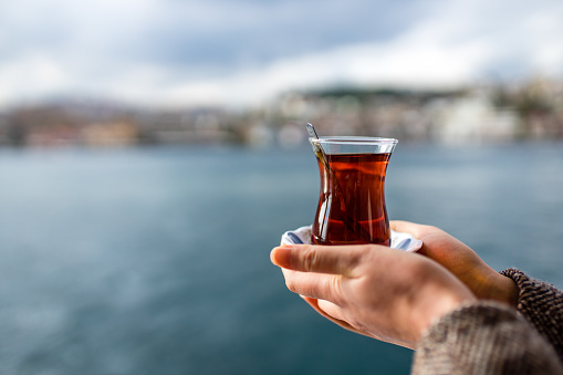 woman drinking Turkish tea in the front, bosphorus bay in the background.