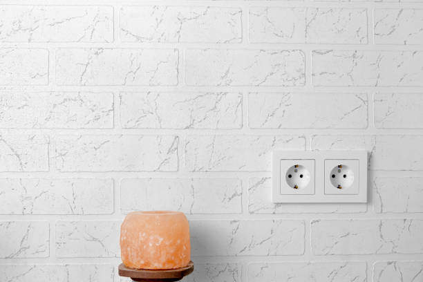 On the white brick wall there is a double white rosette, next to it is a candle-lantern made of salt on a wooden stand. Health