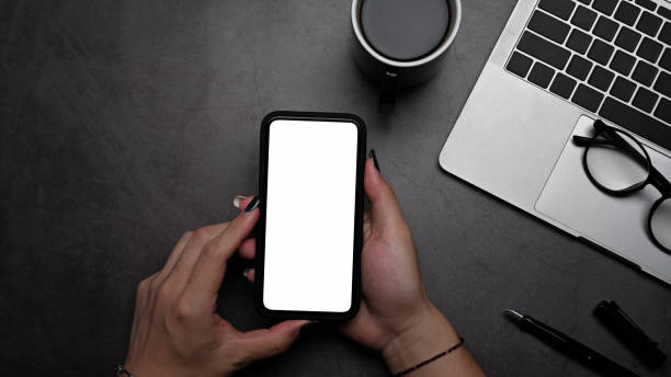 istock Overhead view woman hands holding mobile phone with empty display for graphic display montage. 1392278288