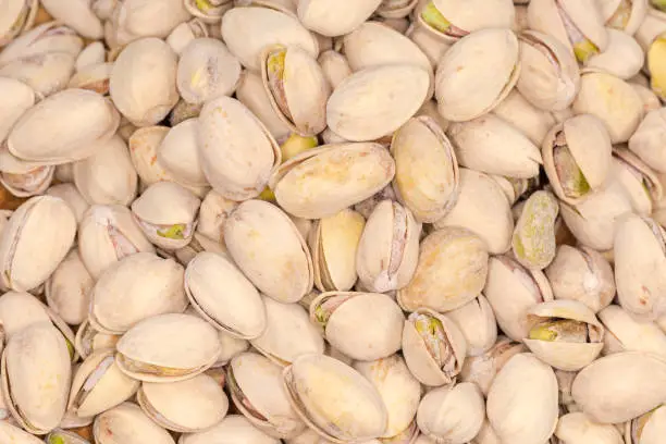 Background of pile of the roasted salted pistachio nuts with partly open shells, top view in selective focus