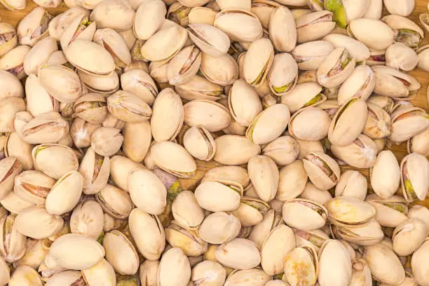Background of the roasted salted pistachio nuts with partly open shells on a wooden surface, top view