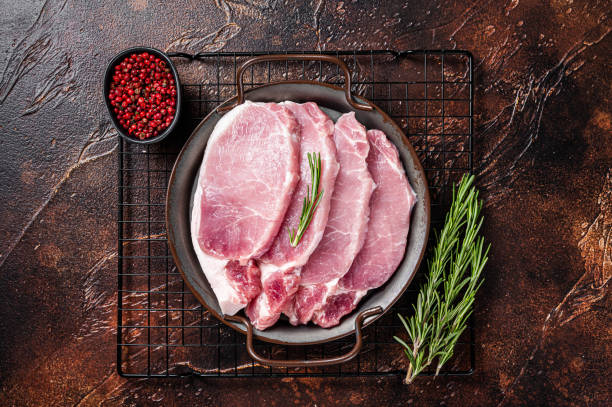 Raw pork chop steaks in steel tray with rosemary. Dark background. Top view Raw pork chop steaks in steel tray with rosemary. Dark background. Top view. cut of meat stock pictures, royalty-free photos & images