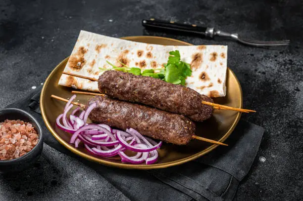 Lamb meat kofta kebab, onion and flat bread on plate. Black background. Top view.