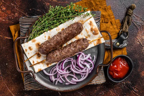 Turkish Adana Kebab from mince lamb beef meat on Skewer with flatbread and onion. Dark background. Top view.