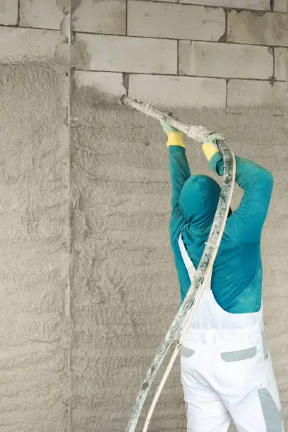 Interior finishing works. The process of applying plaster to walls inside a building by machine. Man applying plaster using a plastering machine station