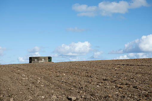Pillbox bomb shelter on the horizon of a ploughed field with a blue cloudy sky