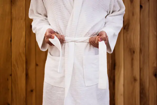 Close up on the hands of a man as he is tying the belt of his bathrobe