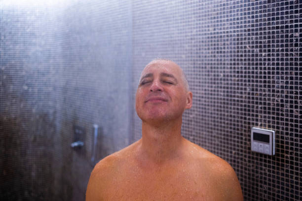A man who takes a shower and washes his hair under water falling from a luxurious shower head. Morning routine luxury lifestyle guy takes a shower. Wellness and spa concept
