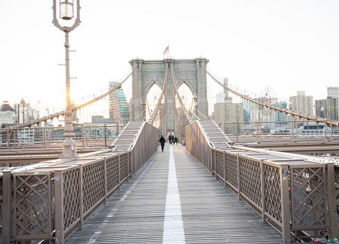 People walking along a footpath on the Brooklyn Bridge on an morning in winter