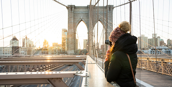 Woman taking photos of the New York skyline from the Brooklyn Bridge on a sunny morning in winter