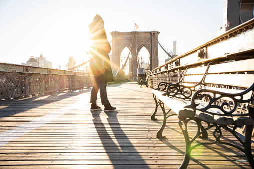 Young woman standing on the footpath of the Brooklyn Bridge during a sunny morning in winter