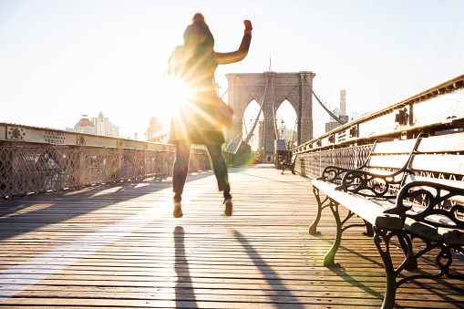Young woman jumping in mid air on a footpath on the Brooklyn Bridge during a sunny morning in winter