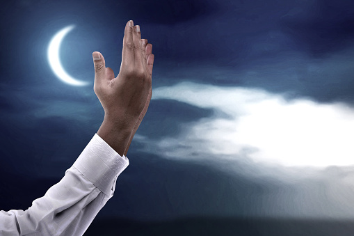 Muslim man standing while raised hands and praying with the night scene background