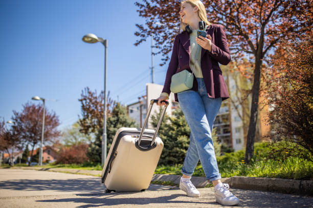 istock Modern Caucasian young woman using mobile phone while travel with suitcase 1392297989