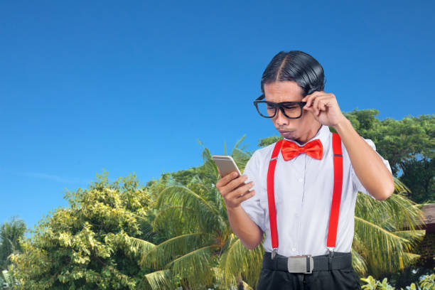 nerd asiático con una cara fea sosteniendo el teléfono móvil - bizarre nerd humor telephone fotografías e imágenes de stock
