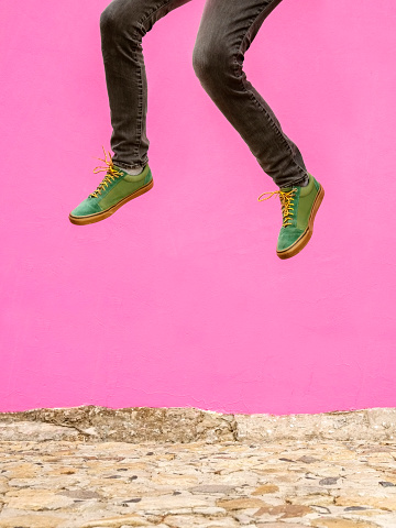 Cropped shot of a man in green sneakers jumping against pink wall