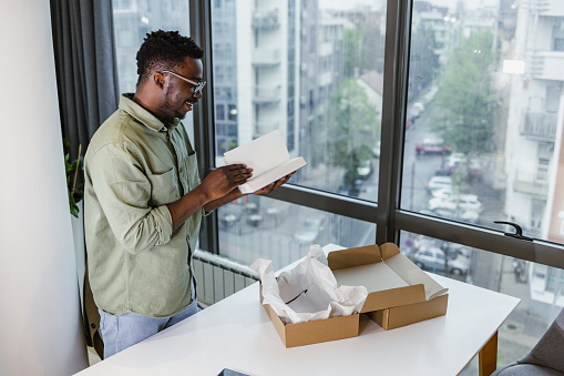 Young man opening a cardboard box package with books.