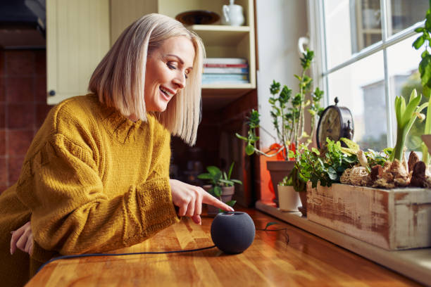 Happy mature woman using smart speaker at home in a kitchen stock photo