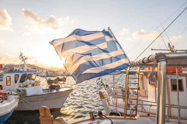 Greek flag on boat, Naoussa harbour, Paros, Greece fishing boats docked at the harbour. paros stock pictures, royalty-free photos & images