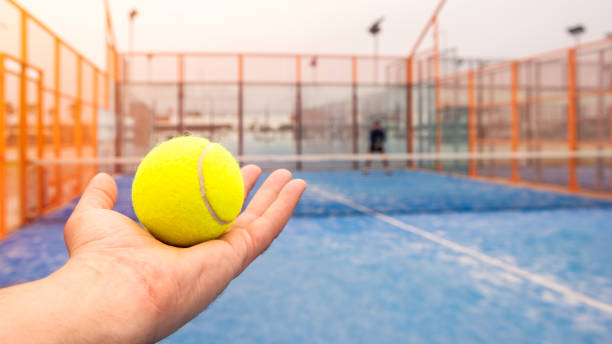 Trainer teaches paddel to student on outdoor tennis court. Man playing padel Trainer teaches paddel to male student on outdoor tennis court. Man playing padel in a blue grass court outdoors behind the net paddle ball stock pictures, royalty-free photos & images