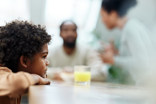 Small African American boy feeling sad while his parents are arguing in the background. Copy space.