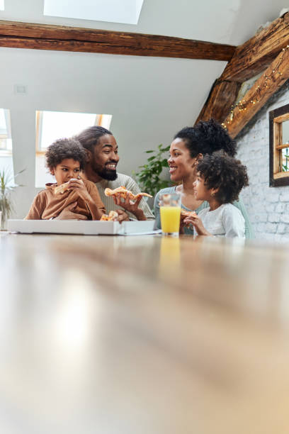happy black family talking while eating pizza for lunch in dining room. - pizza eating african descent lunch imagens e fotografias de stock