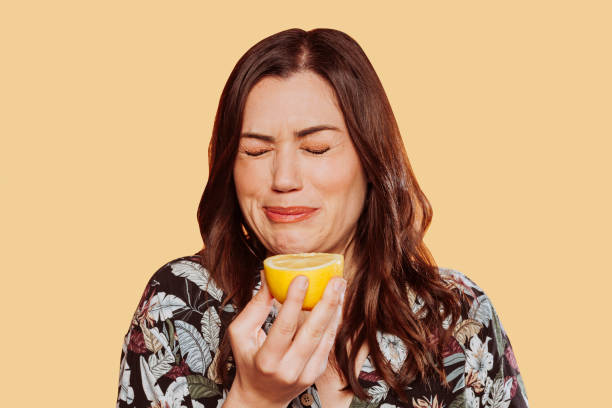Woman eating lemon doing funny face expression Face portrait of woman wears floral shirt, eating acid lemon doing funny face expression with eyes closed. Studio shot over yellow background. sour face stock pictures, royalty-free photos & images