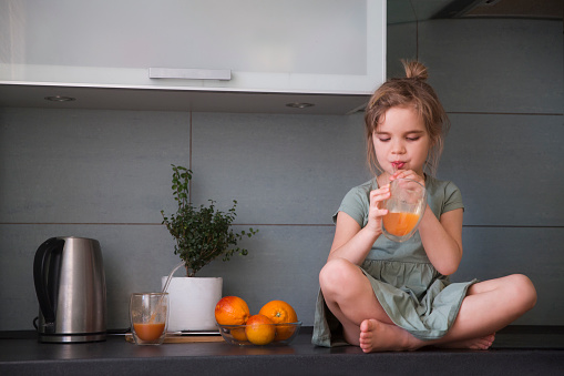 healthy diet. vitamins. little girl drinks juice sitting on a table in the kitchen