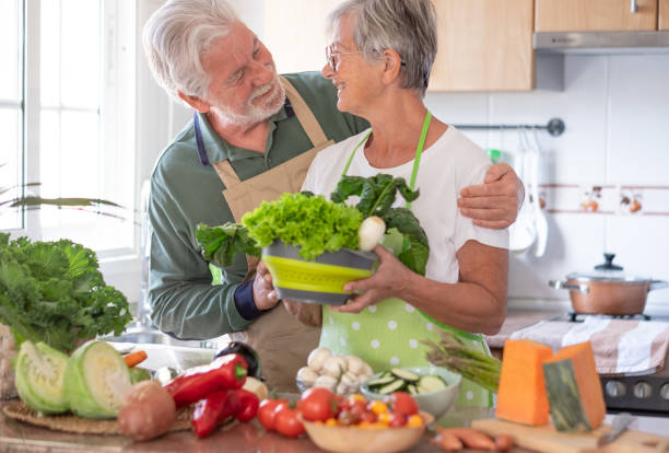 Attractive senior couple working together in home kitchen preparing vegetables. Elderly smiling couple enjoying healthy lifestyle looking in the eyes
