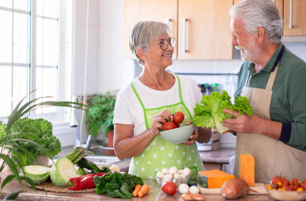 istock Attractive senior couple working together in home kitchen preparing vegetables. Elderly smiling couple enjoying healthy lifestyle looking in the eyes 1392311200