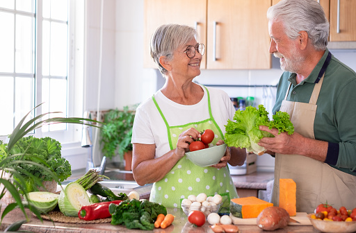 Attractive senior couple working together in home kitchen preparing vegetables. Elderly smiling couple enjoying healthy lifestyle looking in the eyes