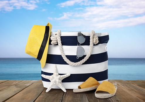 Stylish bag with beach accessories on wooden surface near seashore