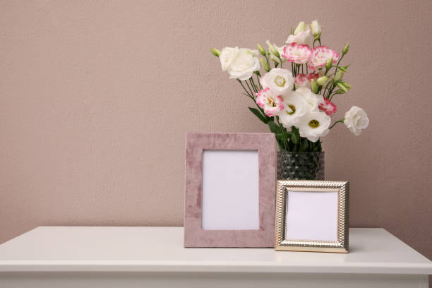 istock Empty photo frames and beautiful bouquet on white table near pink wall, space for text 1392311466