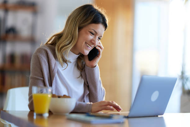 istock Happy woman talking on cell phone while working on laptop at home. 1392313616