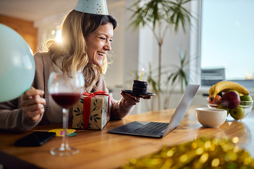 Happy woman celebrating her Birthday while talking to someone through video call at home.