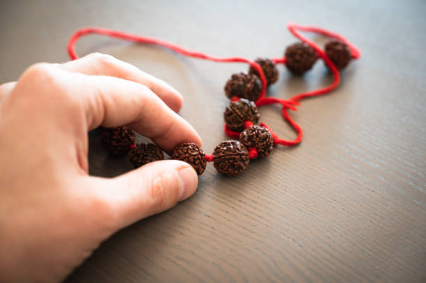 Man's hand holding Rudraksha beads rosary on wooden background.